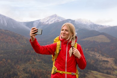 Photo of Happy young woman taking selfie with phone in mountains