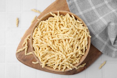 Bowl with uncooked Italian trofie pasta on white tiled table, flat lay