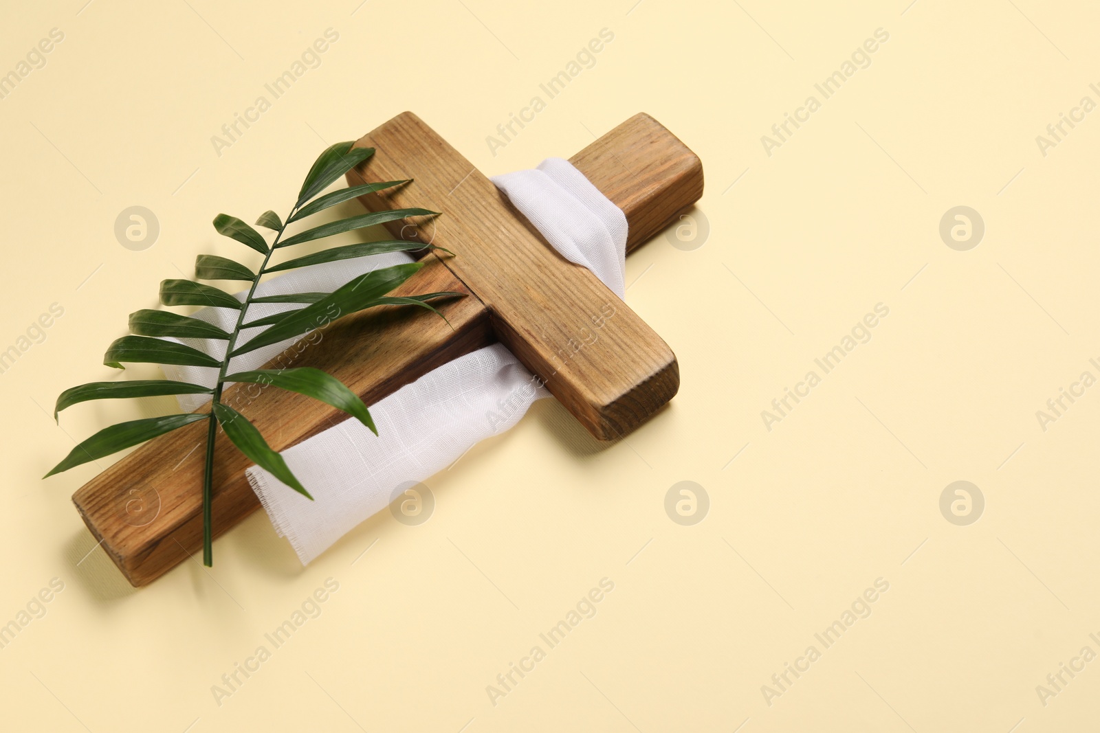 Photo of Wooden cross, white cloth and palm leaf on beige background, space for text. Easter attributes