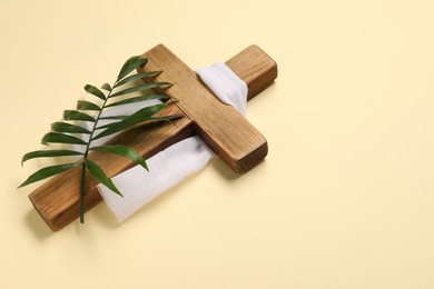 Wooden cross, white cloth and palm leaf on beige background, space for text. Easter attributes