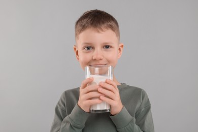 Cute boy with glass of fresh milk on light grey background