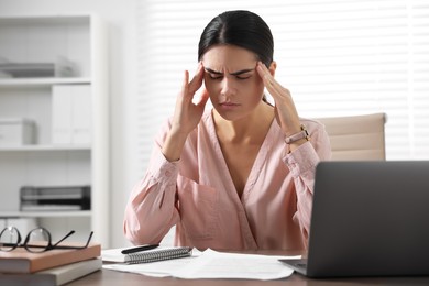 Photo of Young woman suffering from headache at wooden table in office