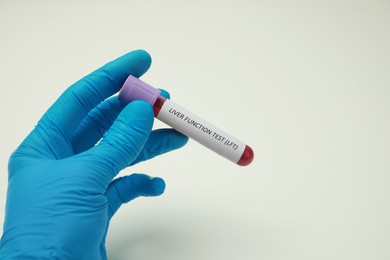 Laboratory worker holding tube with blood sample and label Liver Function Test against white background, closeup. Space for text