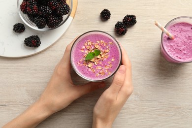 Photo of Woman with glass of delicious blackberry smoothie at white wooden table, top view