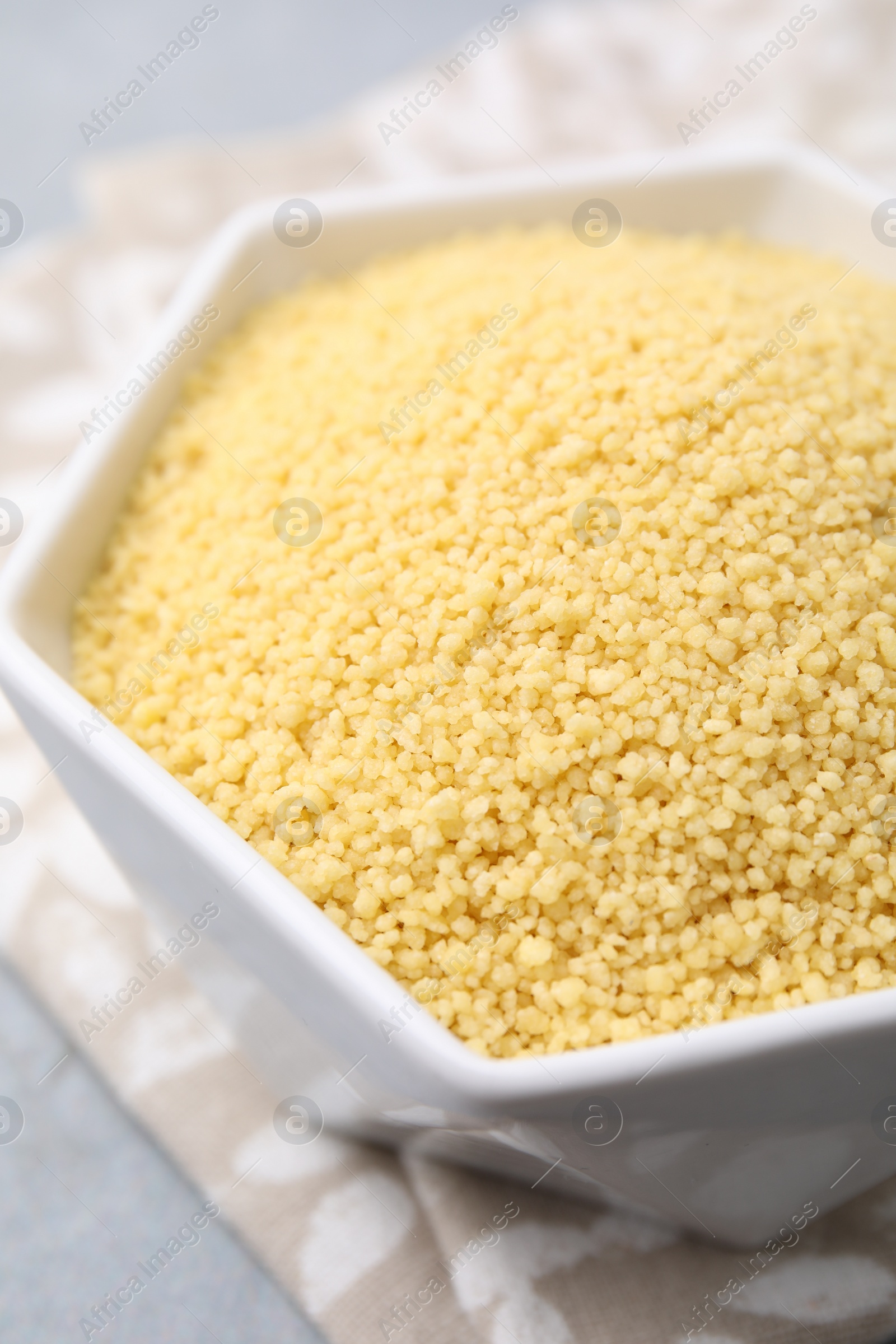 Photo of Raw couscous in bowl on table, closeup