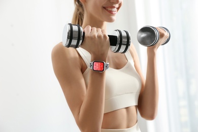 Image of Young woman wearing smart watch during training indoors, closeup
