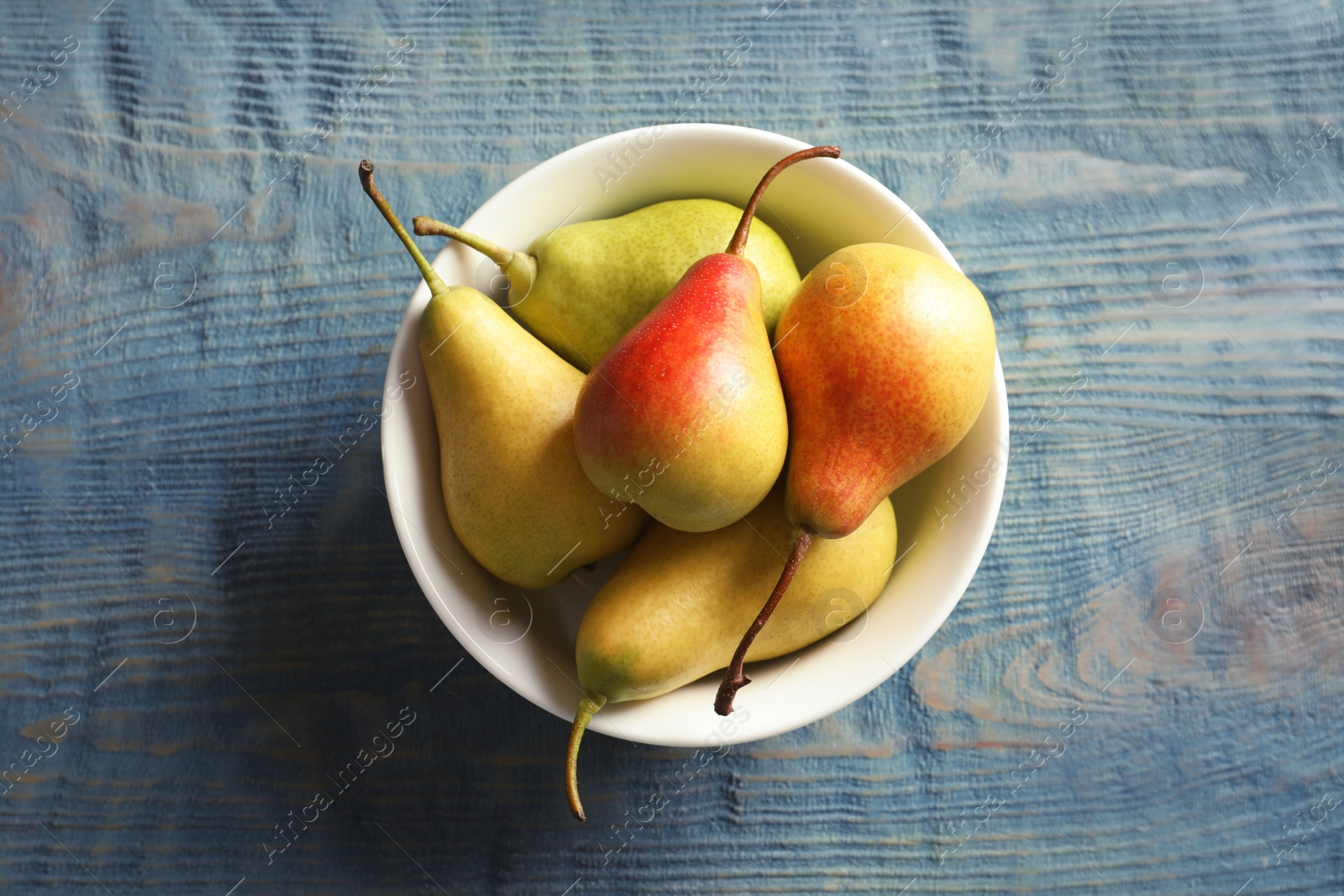 Photo of Bowl with ripe pears on wooden background, top view