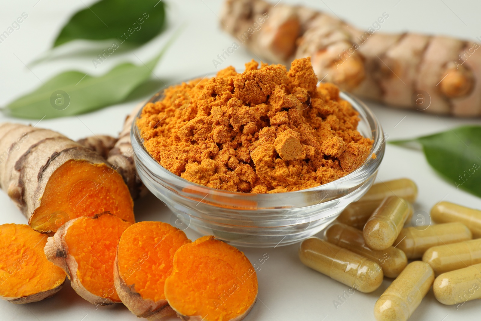 Photo of Aromatic turmeric powder, pills and raw roots on white table, closeup