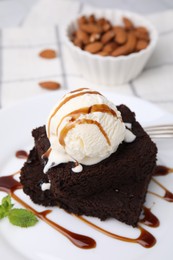 Photo of Tasty brownies served with ice cream and caramel sauce on table, closeup