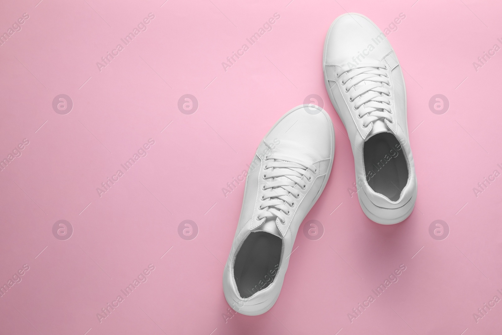 Photo of Pair of stylish white sneakers on pink background, top view. Space for text