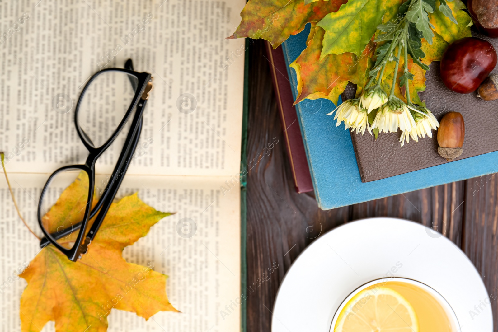 Photo of Maple leaves, books and cup of tea on wooden table, flat lay. Autumn atmosphere