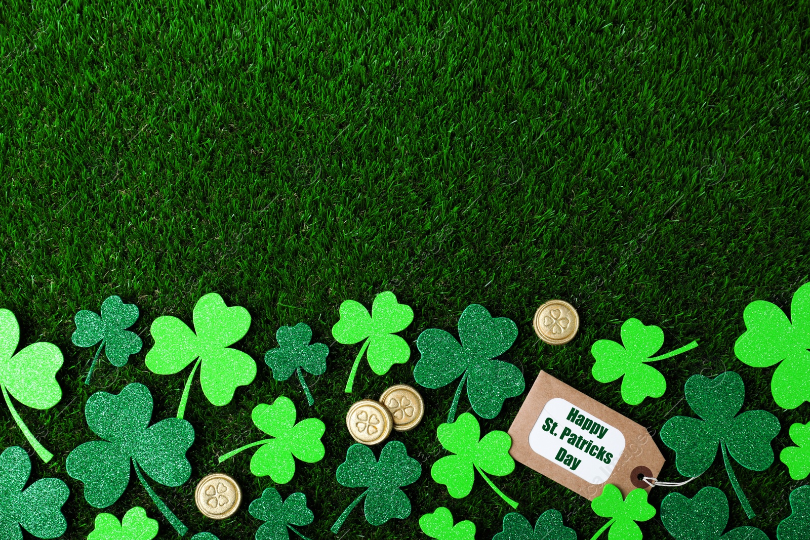 Photo of Flat lay composition with clover leaves and gold coins on green grass, space for text. St. Patrick's Day celebration