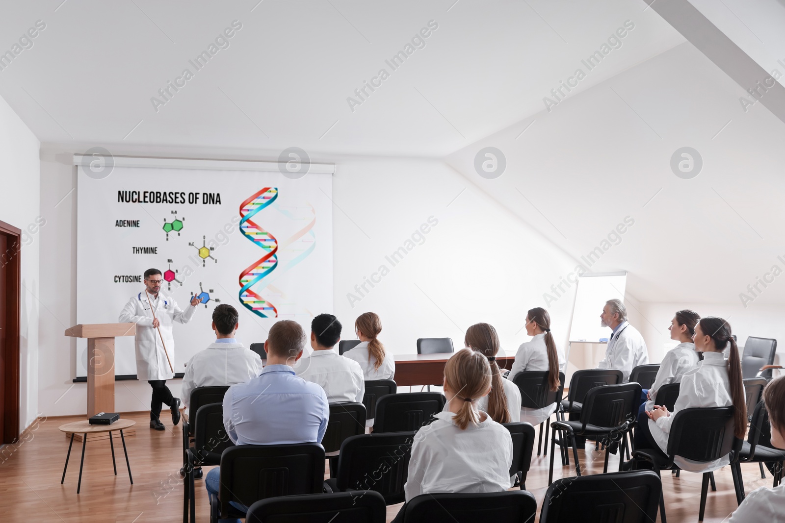 Image of Professor explaining audience nucleobases of DNA during lecture in conference room. Projection screen with illustration