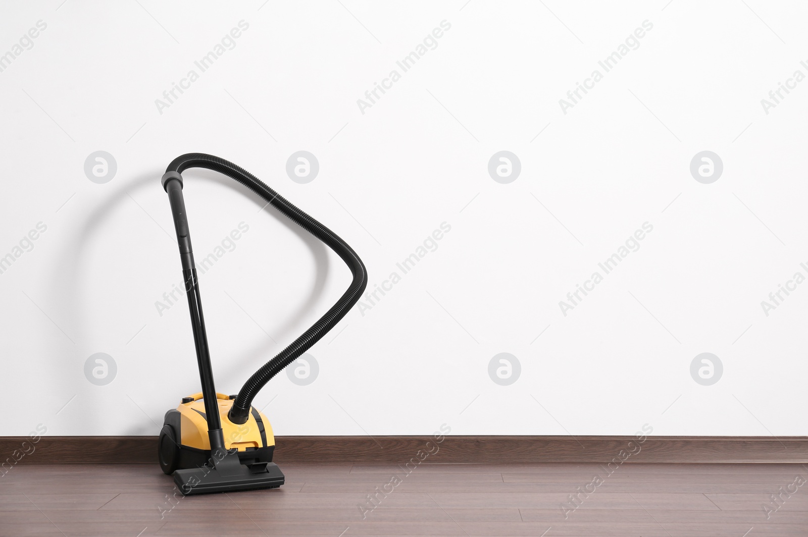 Photo of Modern yellow vacuum cleaner on wooden floor near white wall, space for text