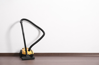 Modern yellow vacuum cleaner on wooden floor near white wall, space for text
