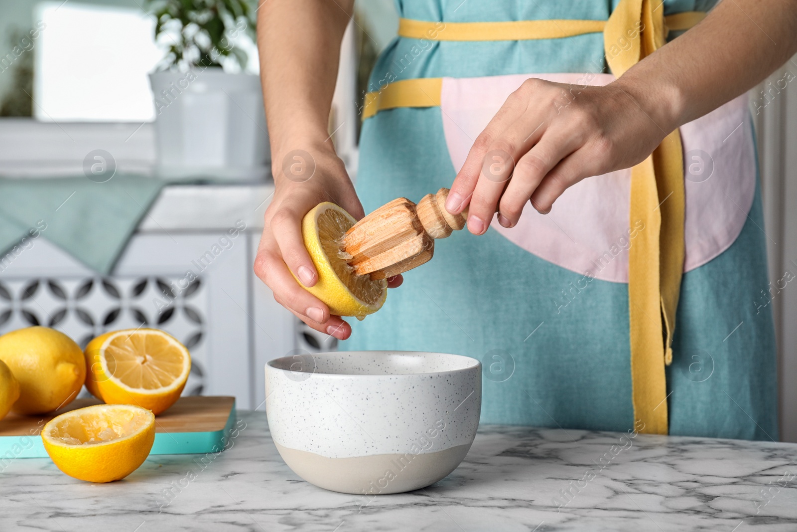 Photo of Woman squeezing fresh lemon juice with wooden reamer into bowl on table
