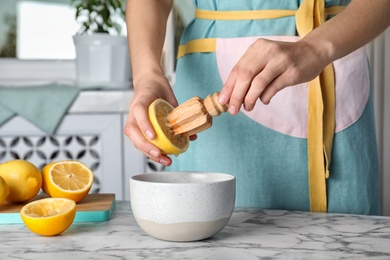 Woman squeezing fresh lemon juice with wooden reamer into bowl on table