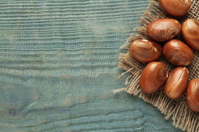 Raw jackfruit seeds and sackcloth on light blue wooden table, flat lay. Space for text