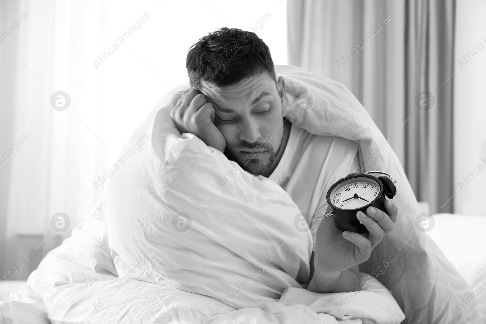 Image of Sleepy man with alarm clock at home in morning. Black and white photography