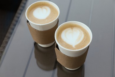 Photo of Paper takeaway cups of coffee with cardboard sleeves on glass table, above view