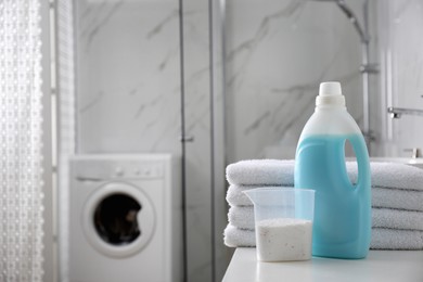 Stack of folded towels and detergents on white table in bathroom, space for text