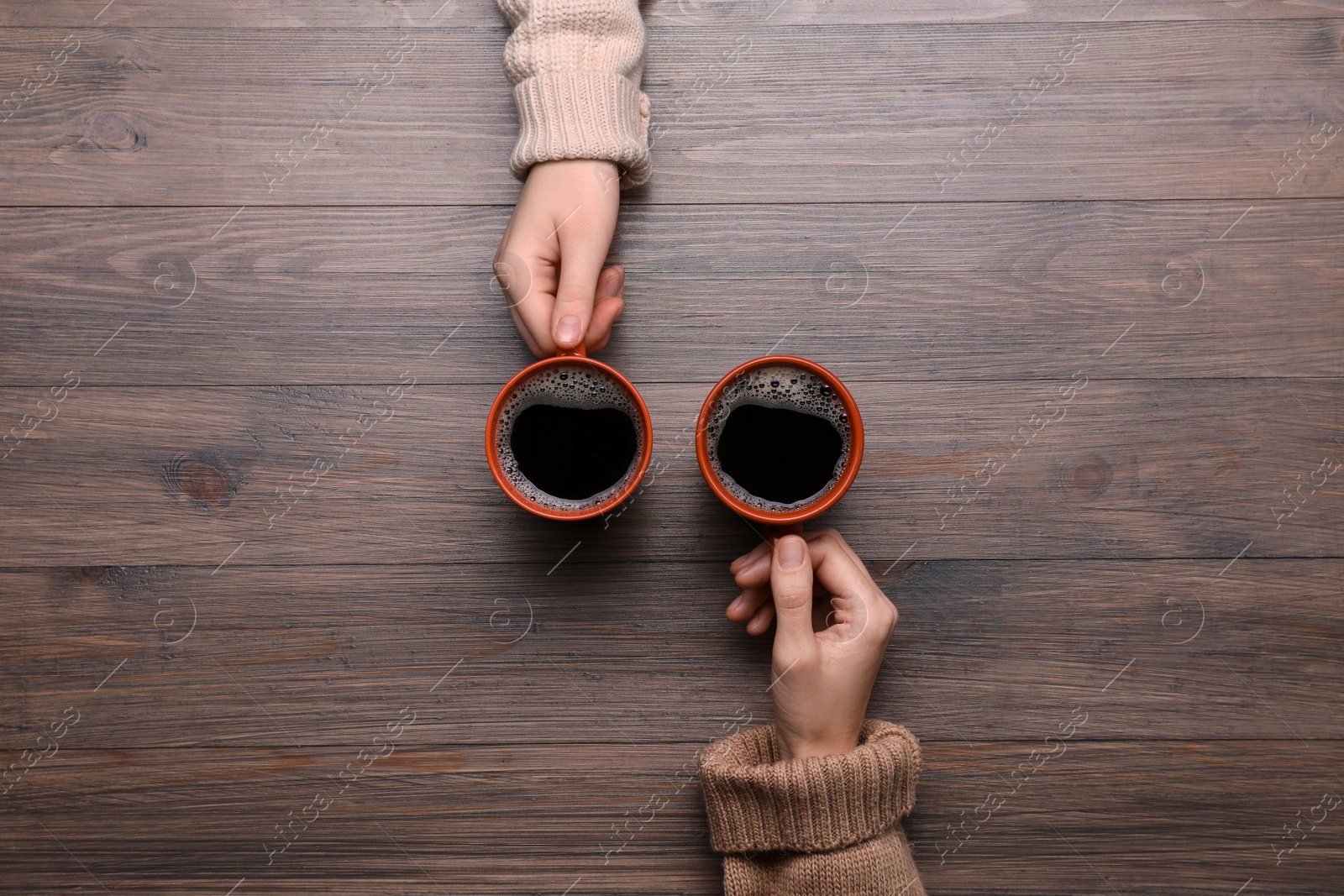 Photo of Women with cups of coffee at wooden table, top view