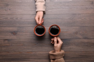 Photo of Women with cups of coffee at wooden table, top view