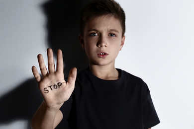 Photo of Abused little boy showing palm with word STOP near white wall. Domestic violence concept