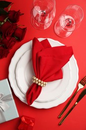 Photo of Place setting with gift boxes and bouquet of roses on red table, flat lay. Romantic dinner