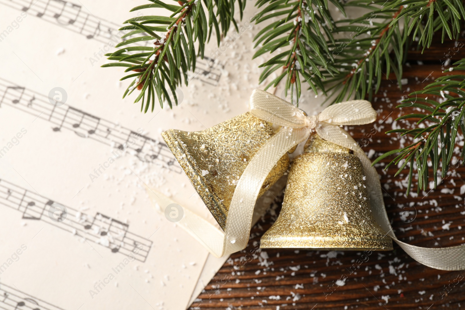 Photo of Golden shiny bells with bow, music sheet and fir branches on wooden table, flat lay. Christmas decoration