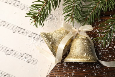 Golden shiny bells with bow, music sheet and fir branches on wooden table, flat lay. Christmas decoration