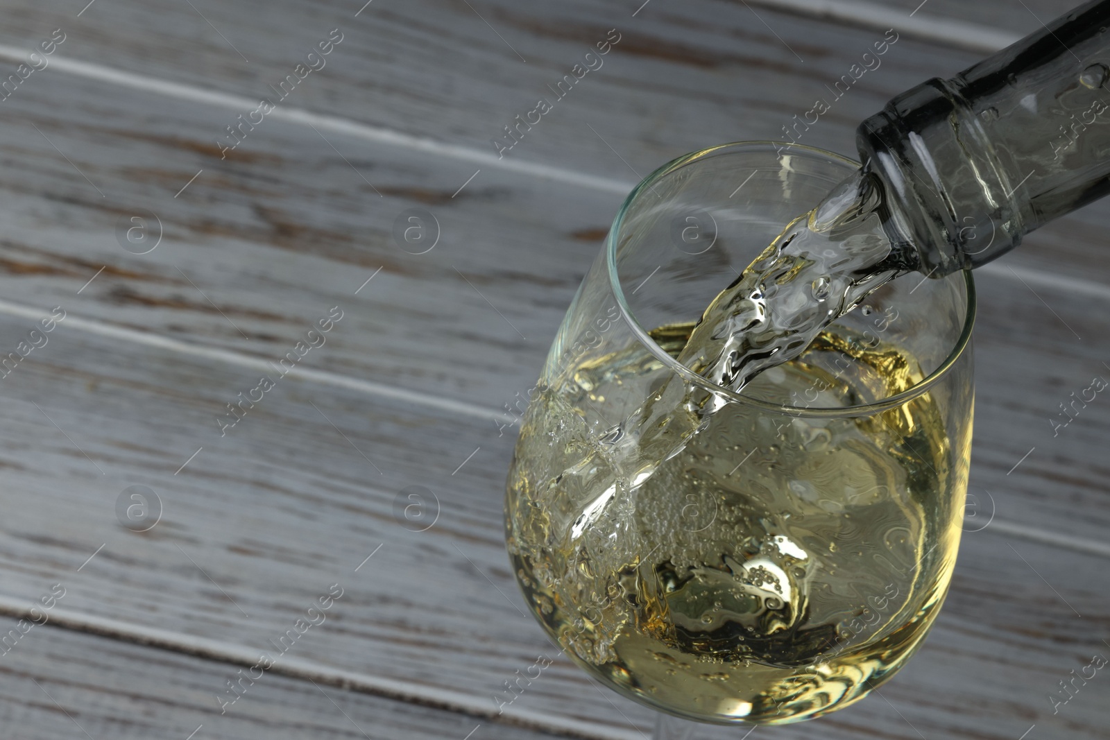 Photo of Pouring tasty aromatic wine in glass at wooden table, closeup. Space for text