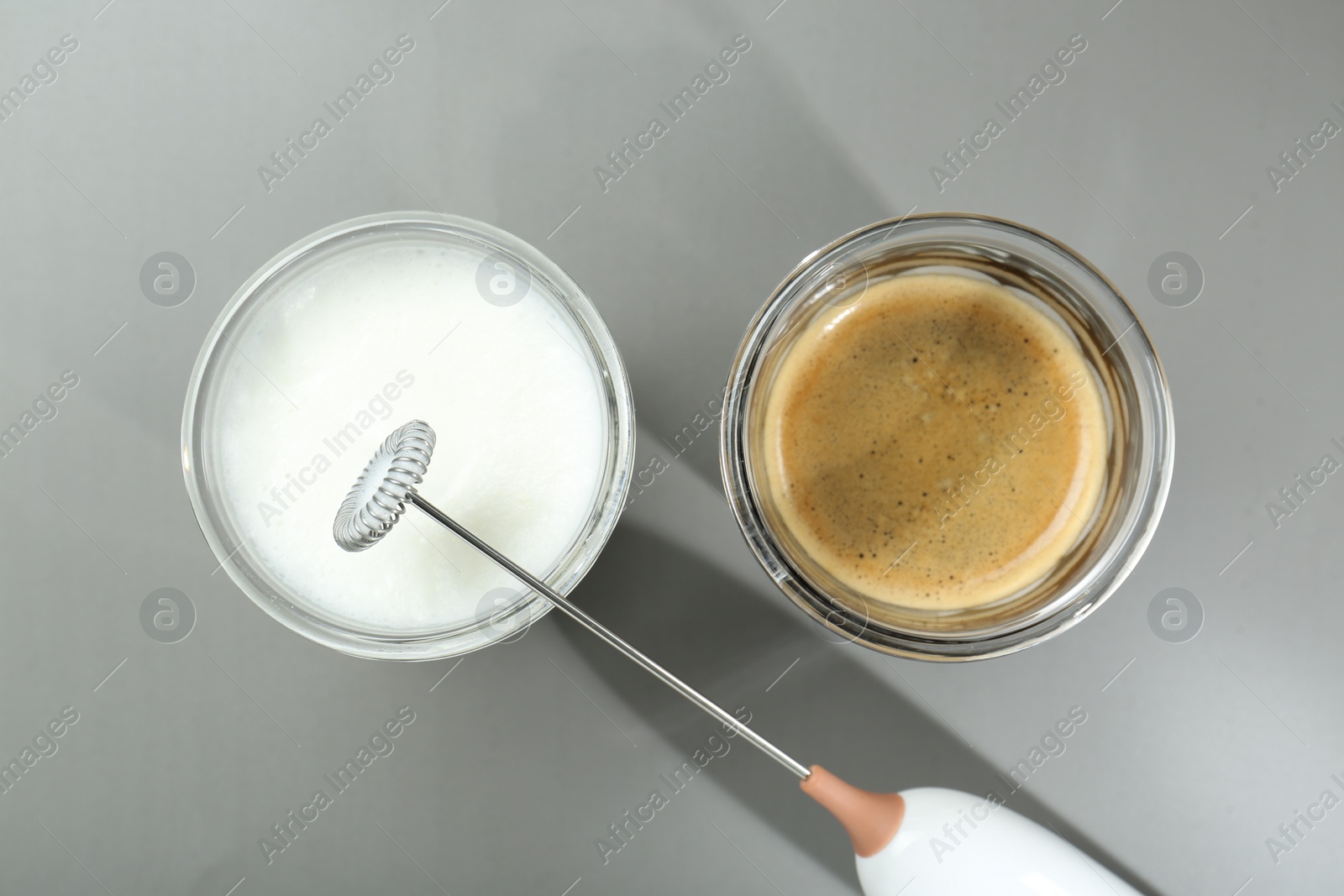 Photo of Mini mixer (milk frother), whipped milk and coffee in glasses on grey background, flat lay