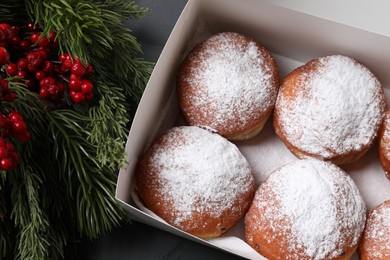 Photo of Delicious sweet buns in box, fir tree branches and red berries on table, flat lay