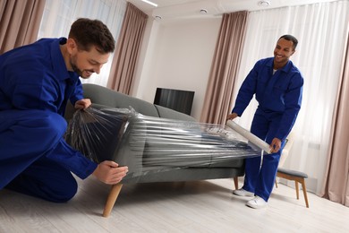 Photo of Male movers with stretch film wrapping sofa in new house