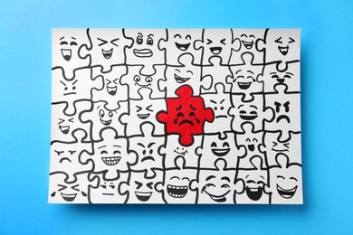 Photo of Drawing of white puzzle pieces and one red with different emotions on turquoise background, top view. Bullying concept