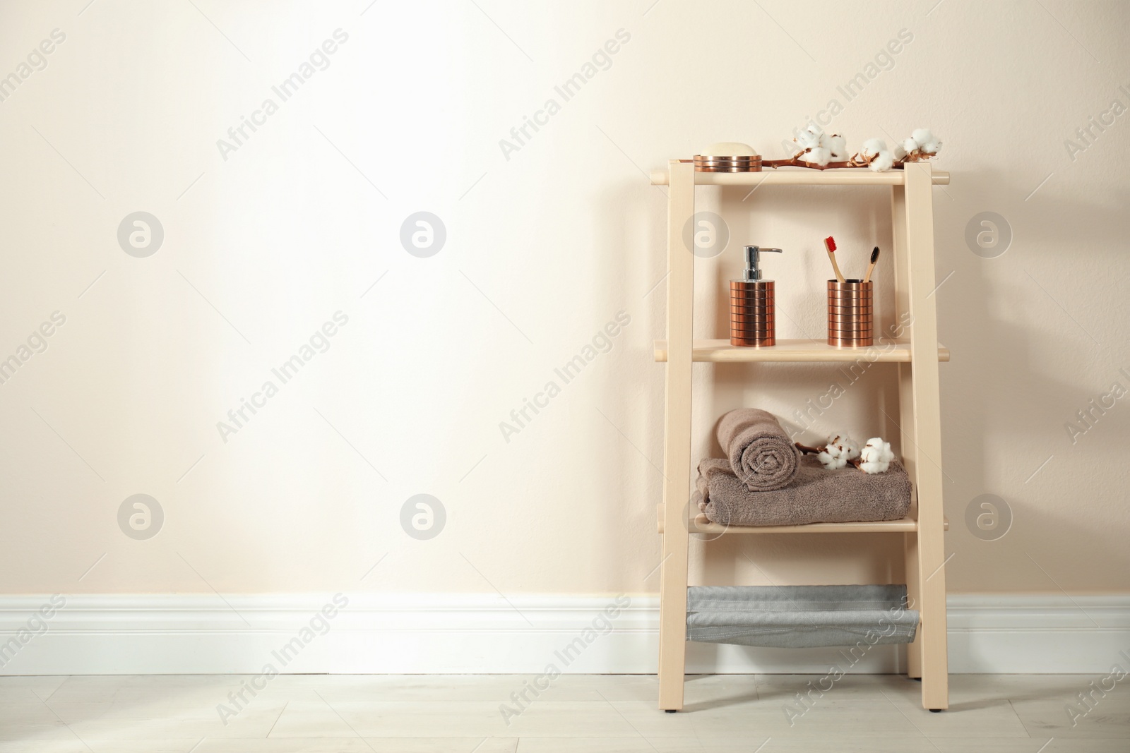 Photo of Wooden shelving unit with toiletries near beige wall indoors, space for text. Bathroom interior element