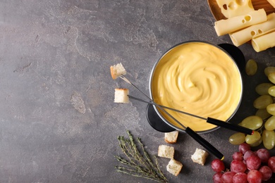 Photo of Flat lay composition with pot of delicious cheese fondue and space for text on gray table