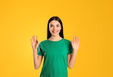 Photo of Attractive young woman showing hello gesture on yellow background