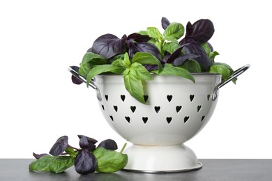 Photo of Colander with fresh basil leaves on grey table against white background