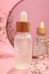 Photo of Bottle of face serum and beautiful flowers near mirror on pink background, closeup