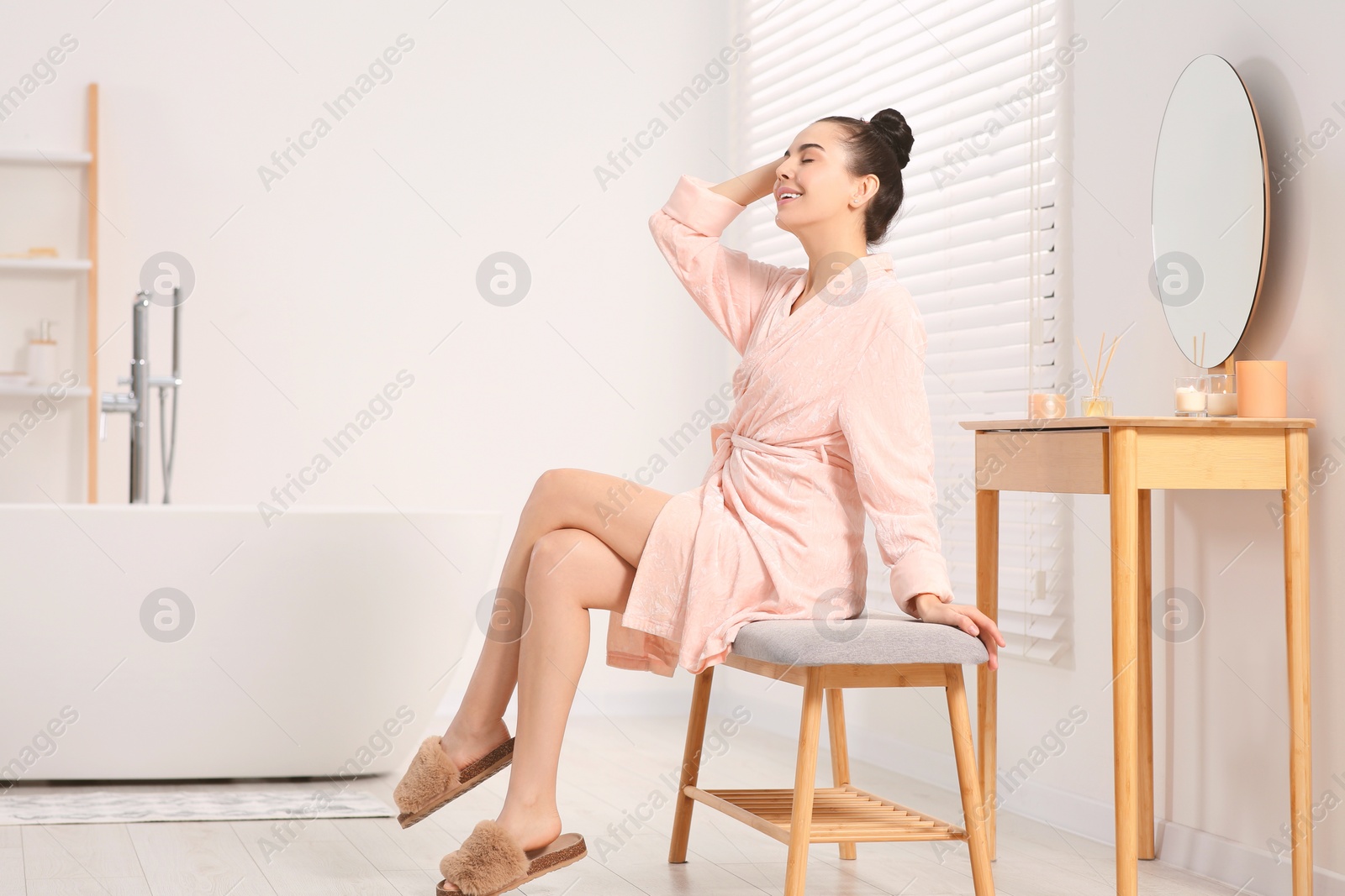 Photo of Beautiful happy woman in stylish bathrobe sitting on bench in bathroom