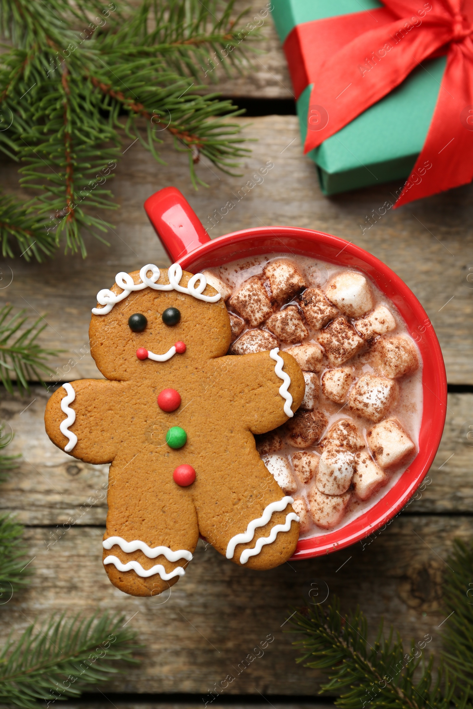 Photo of Tasty Christmas cookie in shape of man, cocoa with marshmallows, gift and fir tree branches on wooden table, flat lay