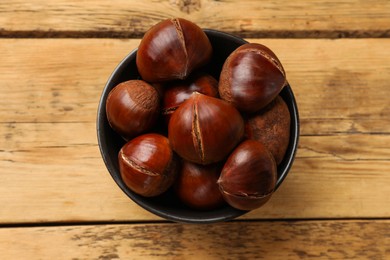 Photo of Fresh edible sweet chestnuts in bowl on wooden table, top view
