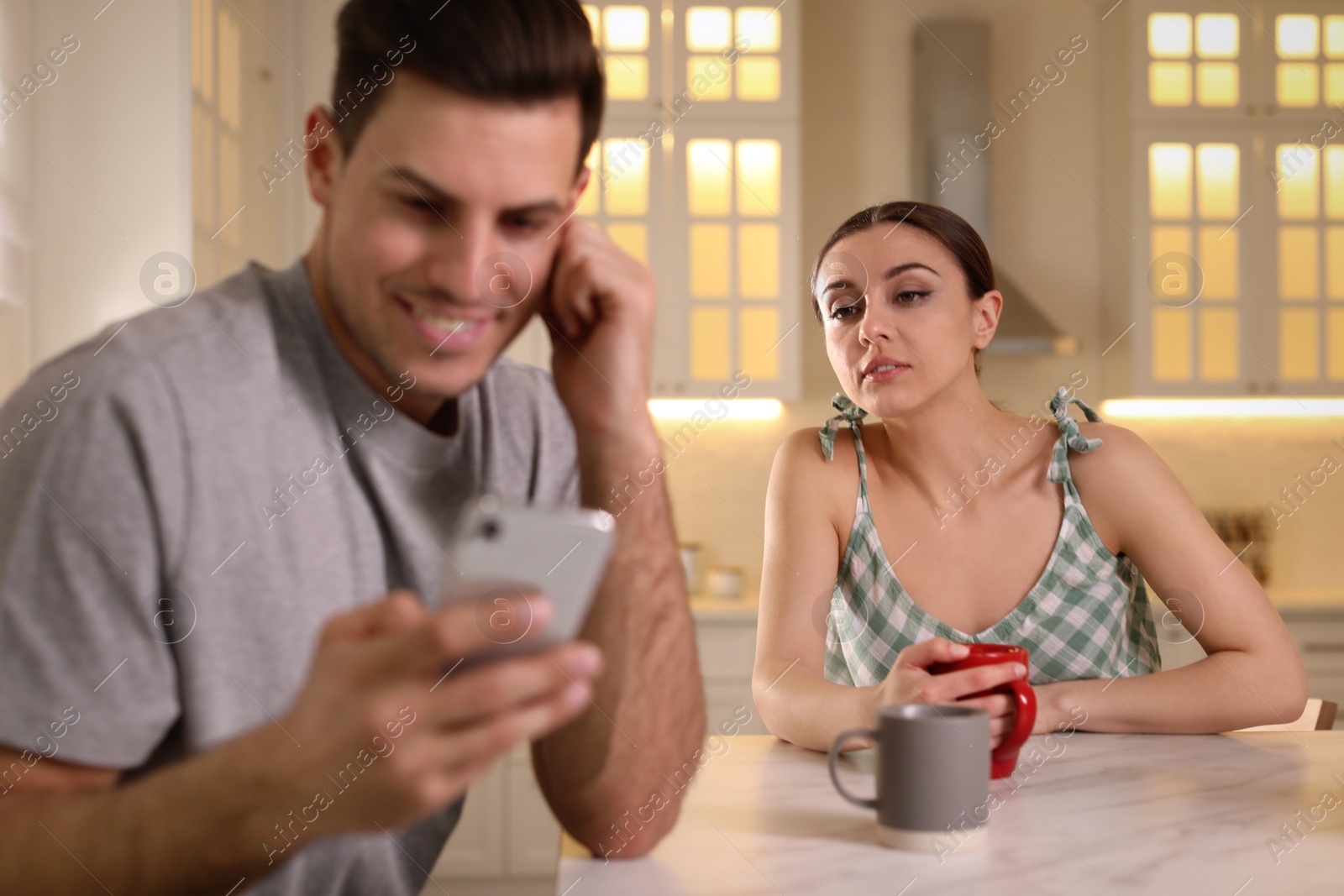 Photo of Distrustful woman peering into boyfriend's smartphone at home. Jealousy in relationship