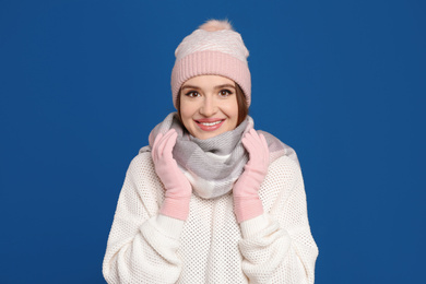 Photo of Young woman wearing warm sweater, gloves, scarf and hat on blue background. Winter season