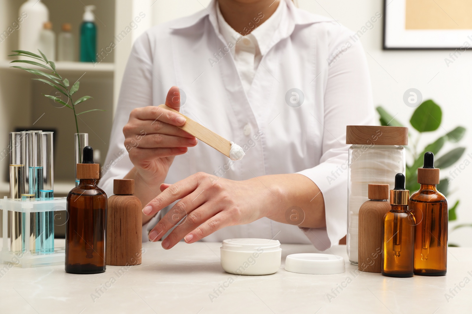 Photo of Dermatologist testing cosmetic product at light marble table indoors, closeup