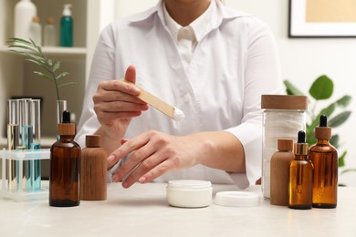 Dermatologist testing cosmetic product at light marble table indoors, closeup