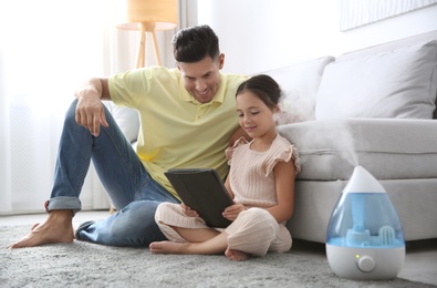 Photo of Father and daughter with tablet near modern air humidifier at home
