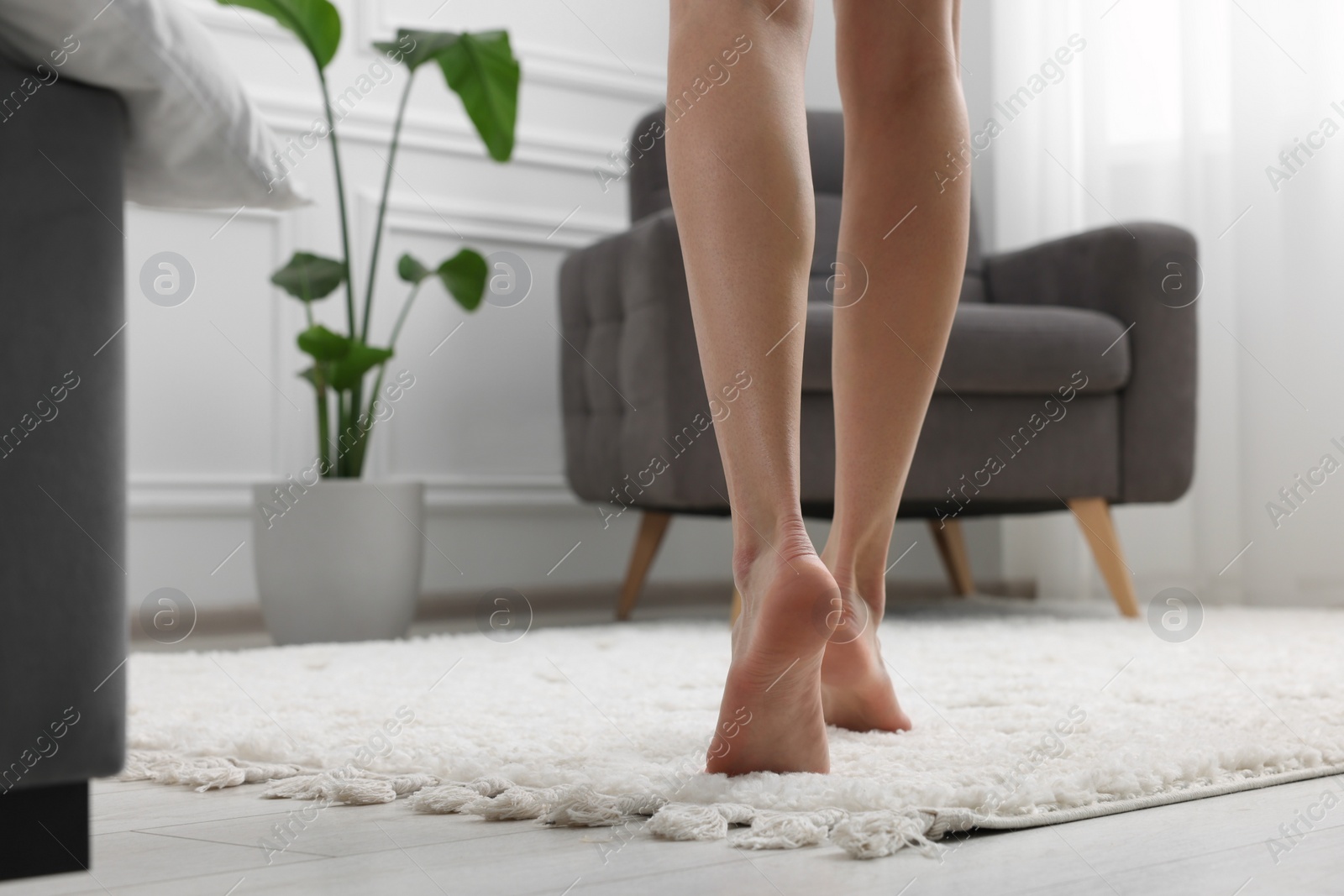 Photo of Woman walking on soft white carpet at home, closeup. Space for text